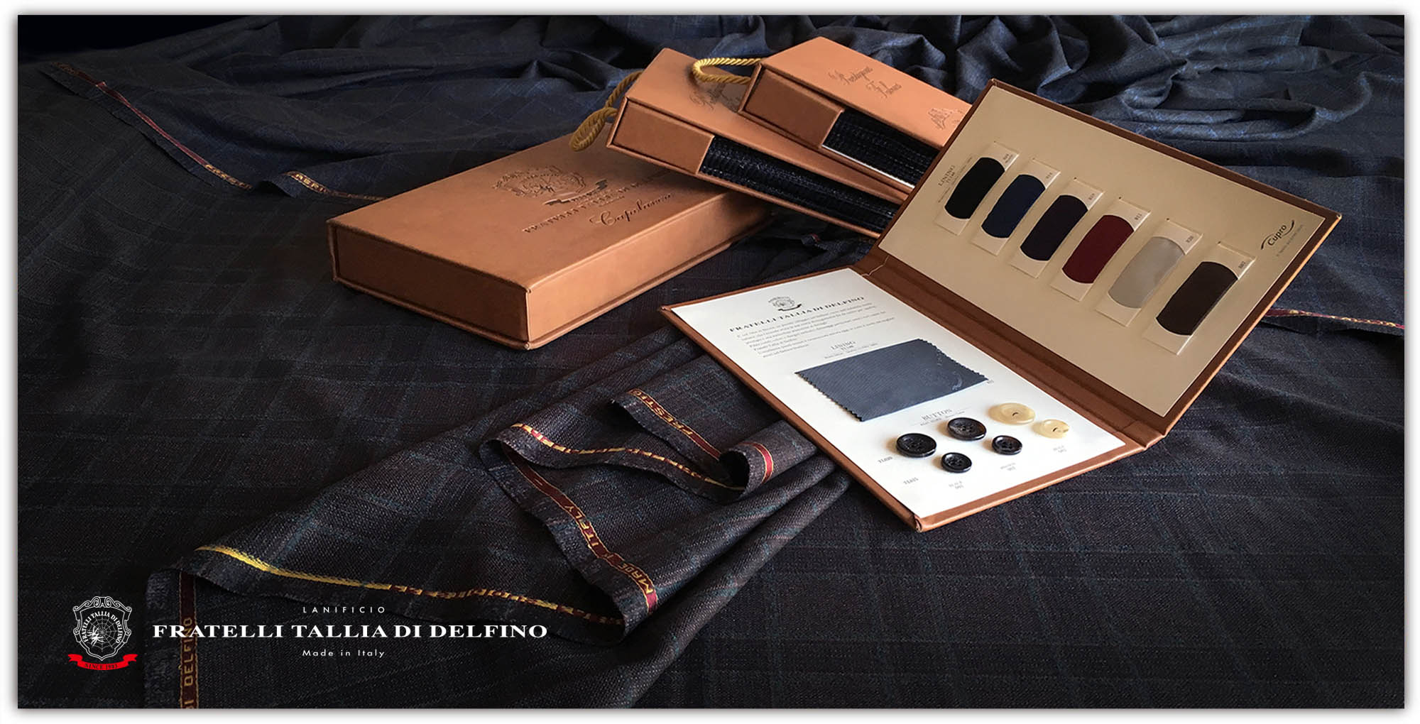 A Fratelli Tallia di Delfino swatch box open on a length of checked suiting cloth
