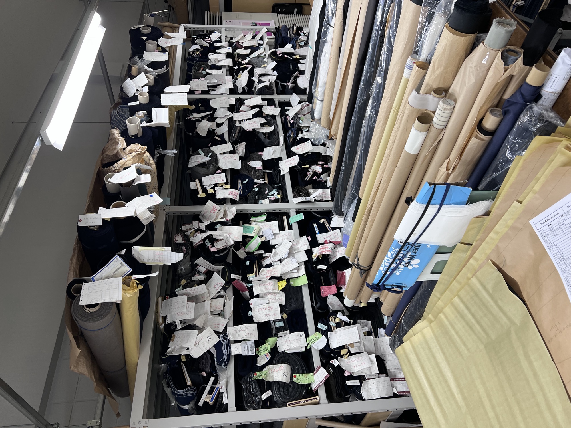The cloth stock room at Five One Factory — rolled suitings tagged with order tickets
